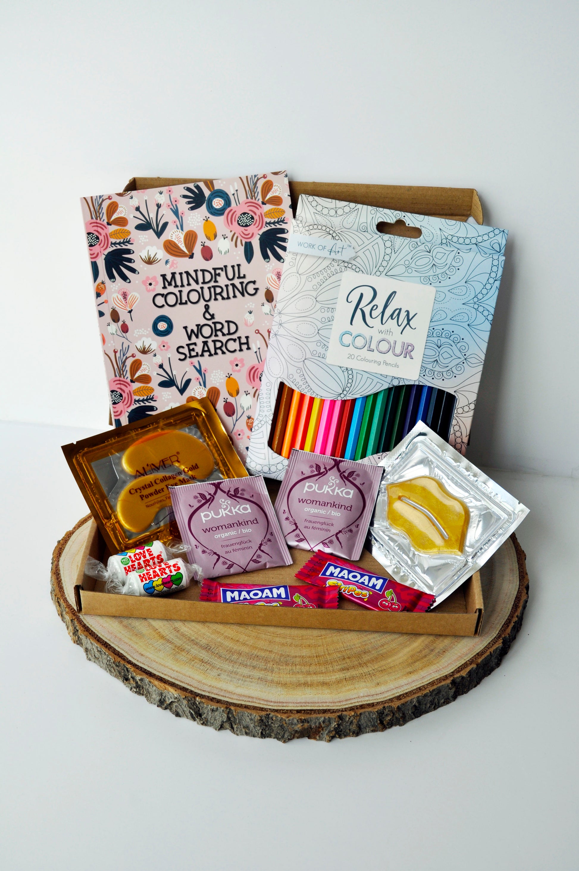 medium letterbox box showing 1 mindful colouring and word search book, 1 set of 20 penbils, 2 maoam sweets, 2 love heart sweets, 2 pukka womenkind sweets. 1 gold collagen eye mask, 1 lip mask