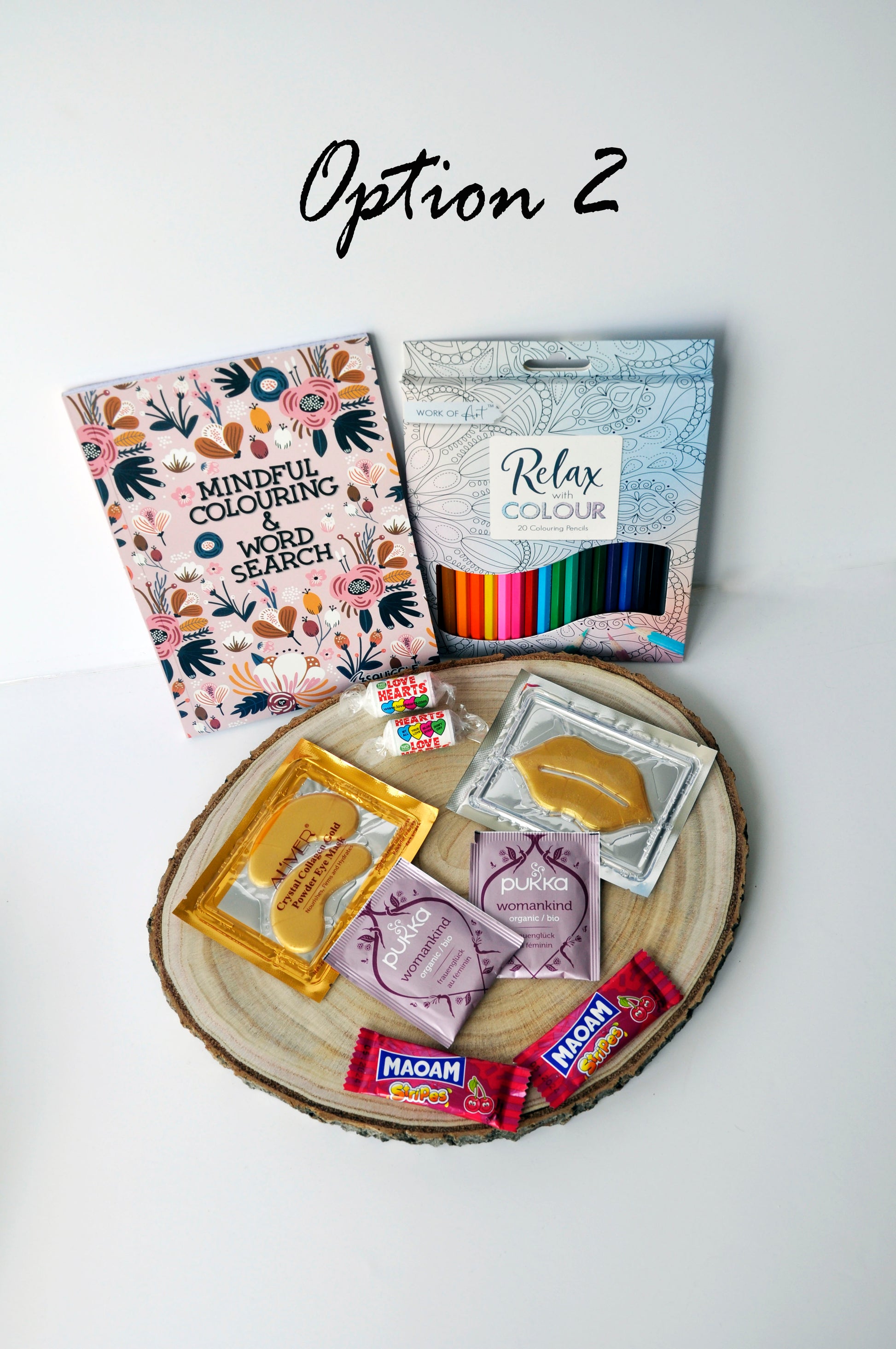 shown are 1 mindful colouring and word search book in pink, 1 set of 20 colouring pencils, 2 love heart sweets, 1 gold collagen eye mask, 1 lip mask, 2 pukka womenkind organic teas, 2 maoam sweets